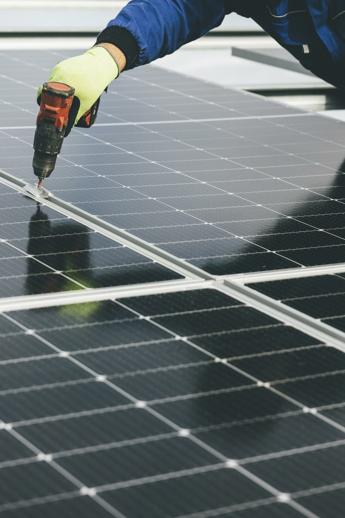 Person Wearing Gloves Holding a Power Tool on a Solar Panel
